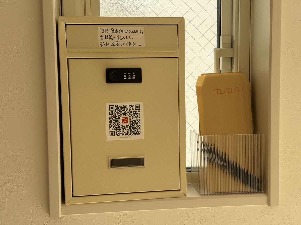 玄関の窓際にある支払い用のポスト。PayPayのQRコードが貼られ、横に封筒がある